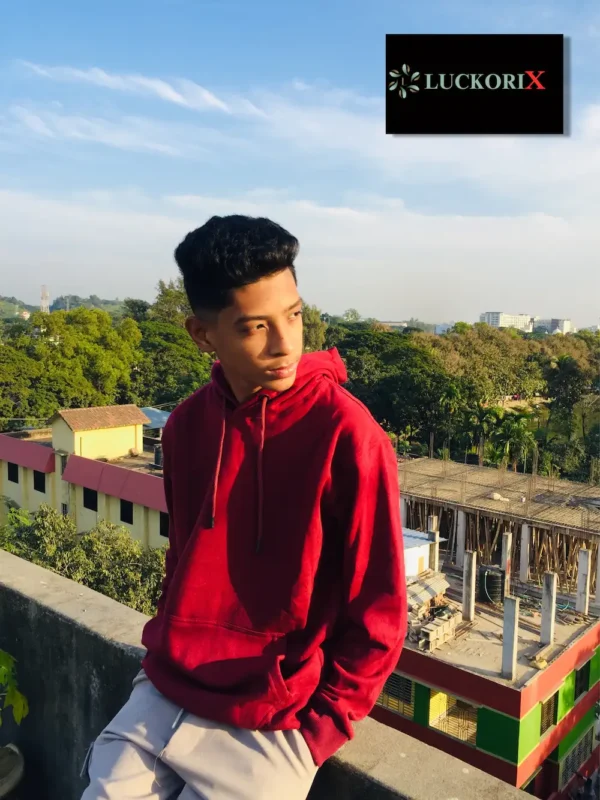 Man wearing a red hoodie by LuckoriX, standing against an urban backdrop, highlighting contemporary fashion.