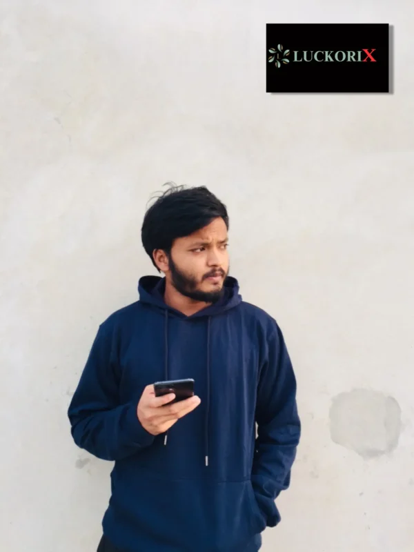 A young man wearing a navy blue hoodie standing confidently on a rooftop with lush greenery and a clear sky in the background. Styled by LuckoriX.