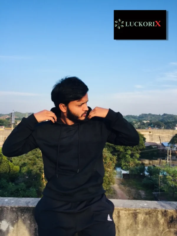 Man wearing a stylish black hoodie, standing on a rooftop with a serene landscape in the background.