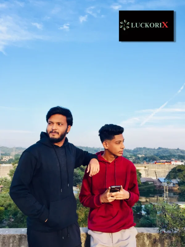 Two men showcasing trendy streetwear hoodies, one in classic black and the other in vibrant red, against a scenic background.