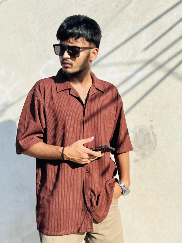 "Stylish man wearing a LuckoriX brown textured shirt, holding phone and posing in natural sunlight"